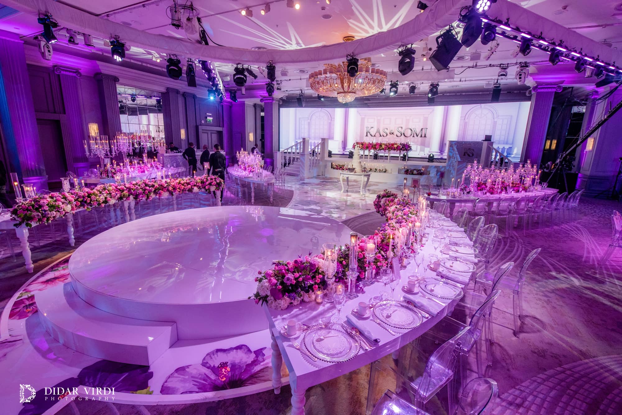 Curved dining tables wrap around a white circular first-dance stage, with a floral walkway leading to the Grosvenor House wedding set.