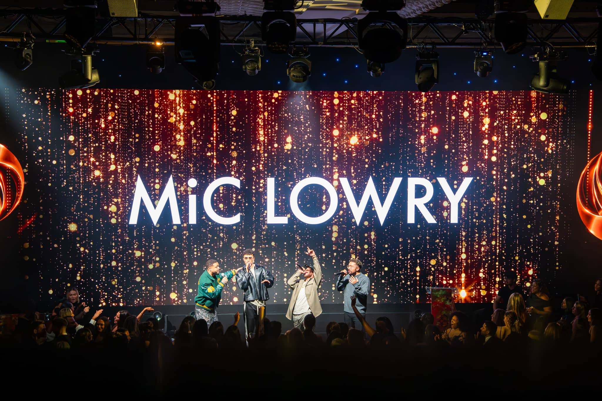 MiC LOWRY performing in front of the LED wall carrying their name, guests gathered at the stage, Dental Beauty Partners Awards 2025 in the Great Room at Grosvenor House London, by Kudos AV.