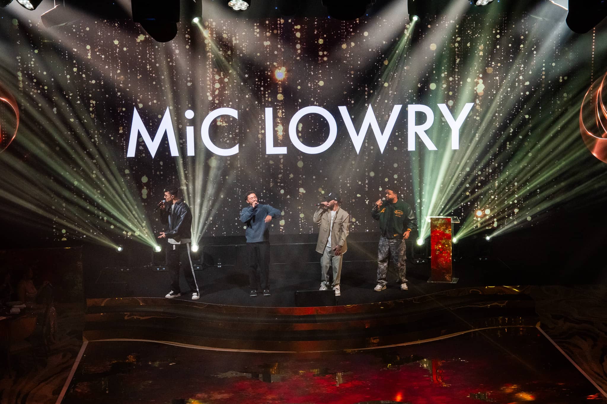 MiC LOWRY on stage under green and white beams, their name on the LED screen behind, Dental Beauty Partners Awards 2025 at Grosvenor House London, by Kudos AV.