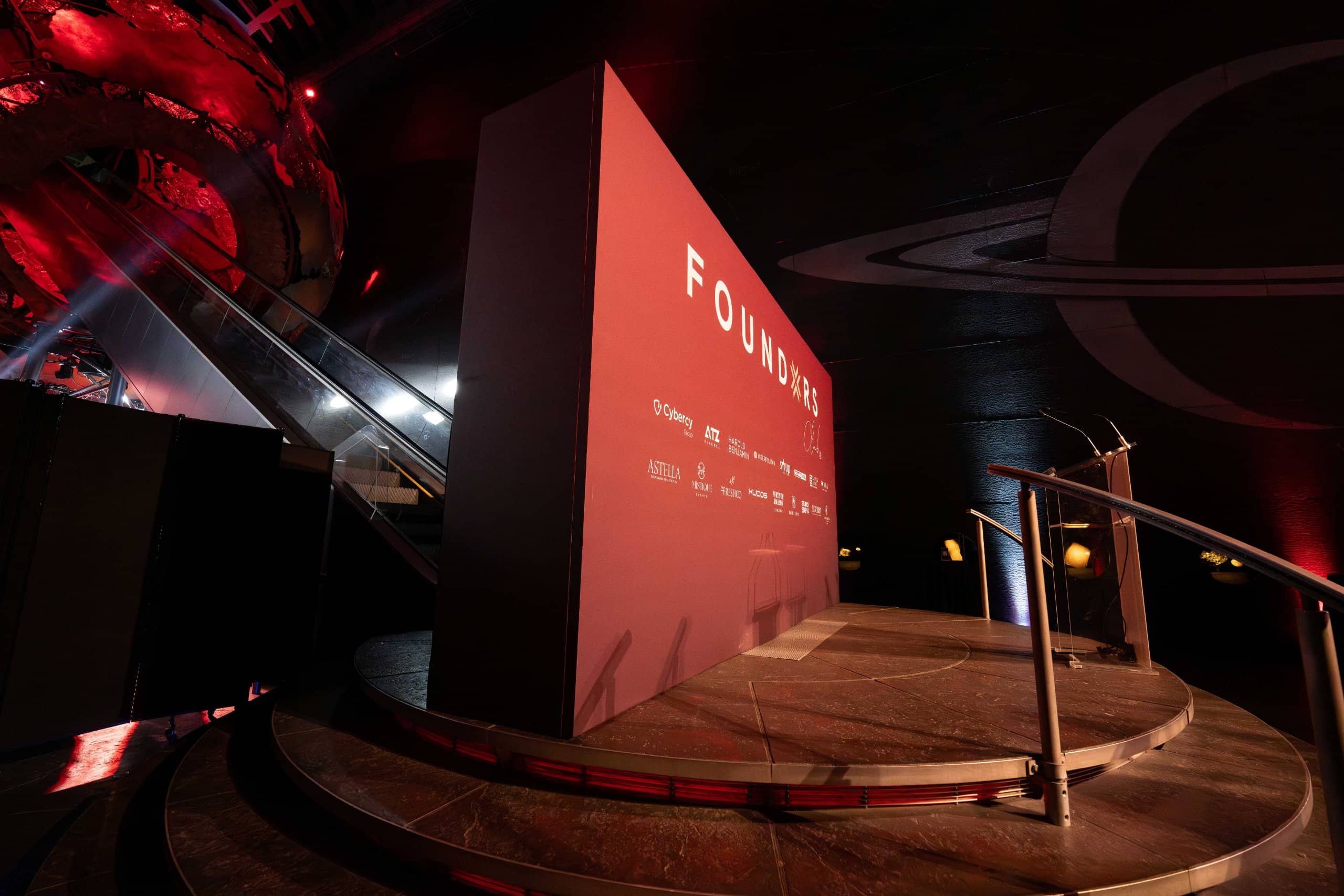 The curved stage and the screen in red for the FOUNDXRS Club black tie party in Earth Hall at the Natural History Museum, by Kudos AV.