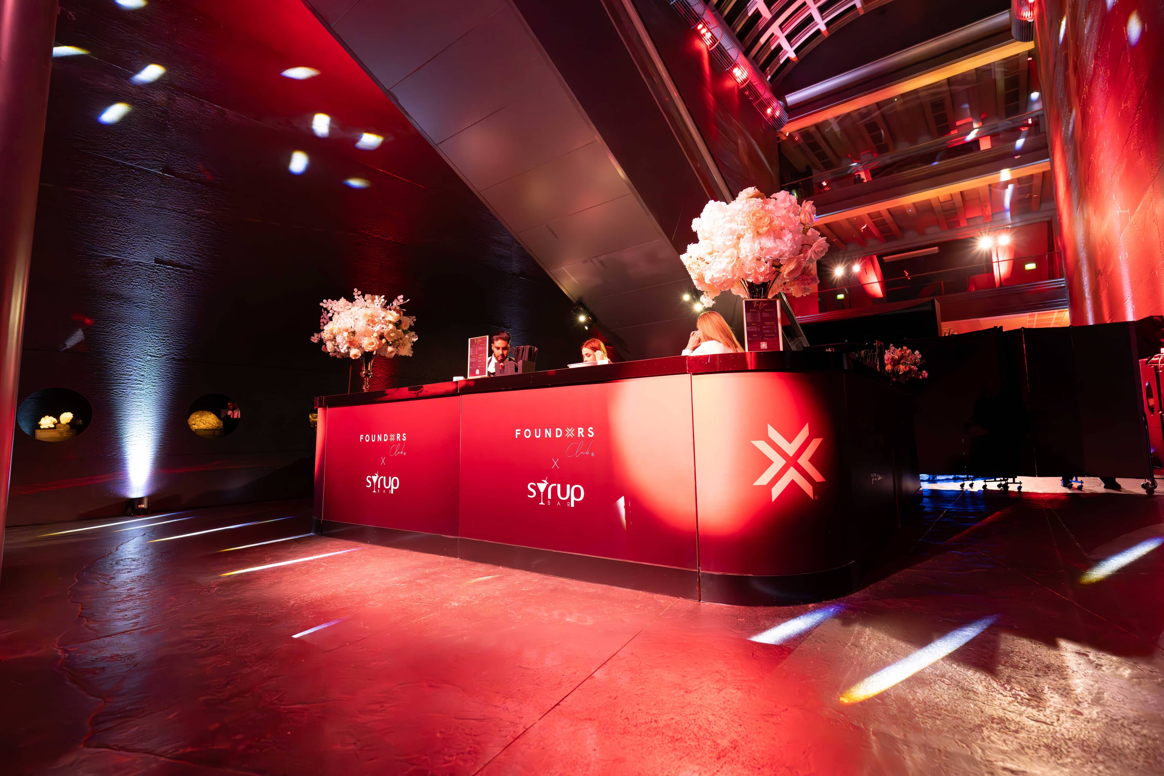 The red lit bar with florals and FOUNDXRS branding at the FOUNDXRS Club black tie party in Earth Hall, by Kudos AV.