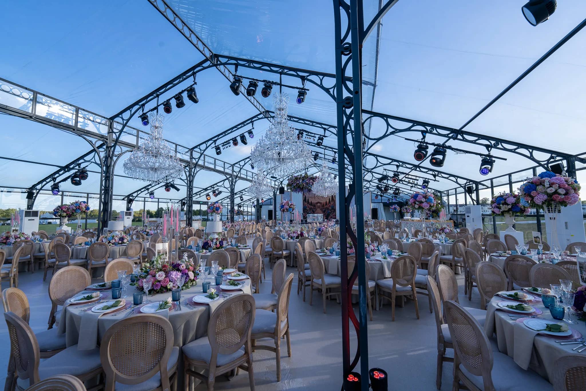 Wildflower centrepieces on the round tables, crystal chandeliers and moving lights rigged on the black frame of a glass marquee at Dallas Burston Polo Club, by Kudos AV