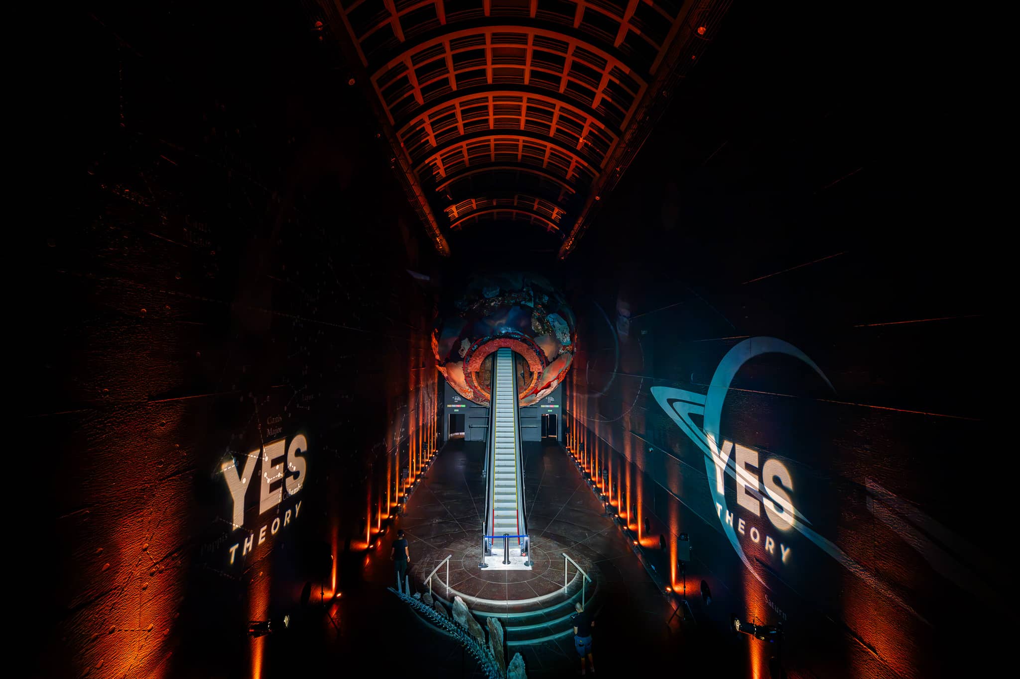 Yes Theory projected on the walls of Earth Hall with amber uplighting and blue accents around the Earth sculpture, by Kudos AV.
