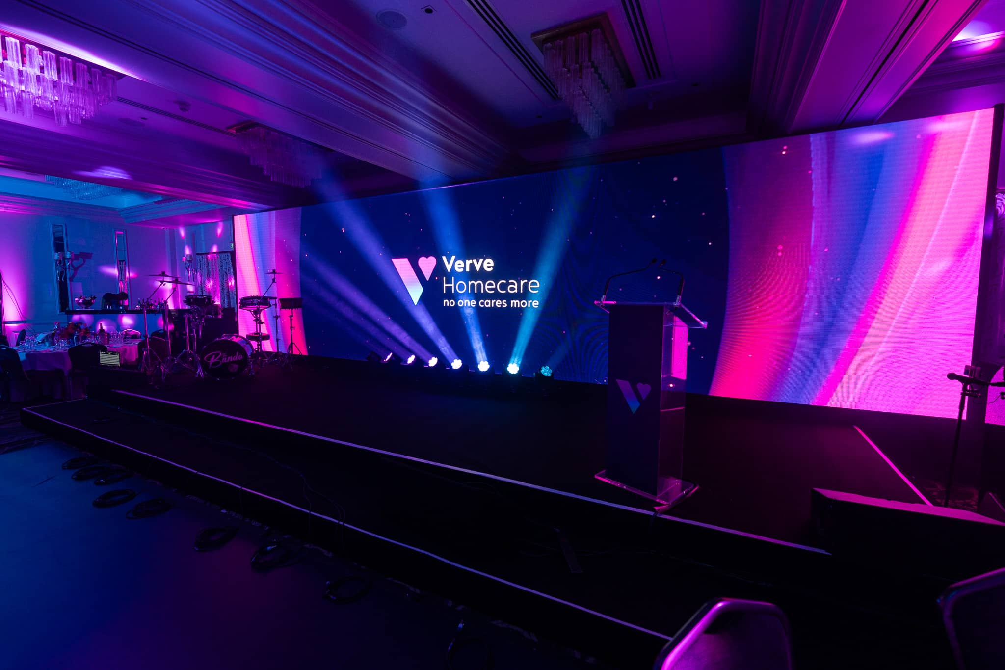 The Verve Awards Night stage with the live band backline behind the lectern and blue beams across the LED wall at Sopwell House.