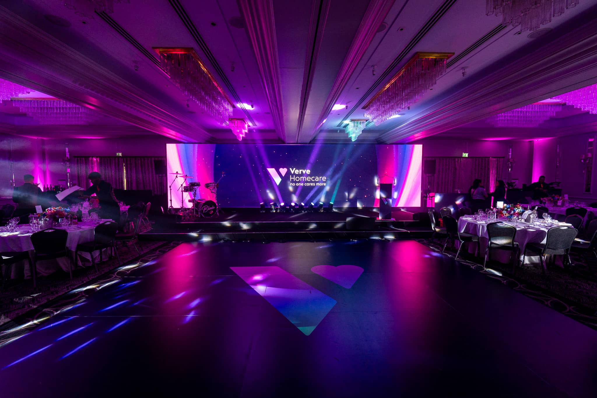 The branded dancefloor with the Verve logo under magenta and blue light, looking towards the LED wall and stage in the St Alban Suite, Sopwell House.