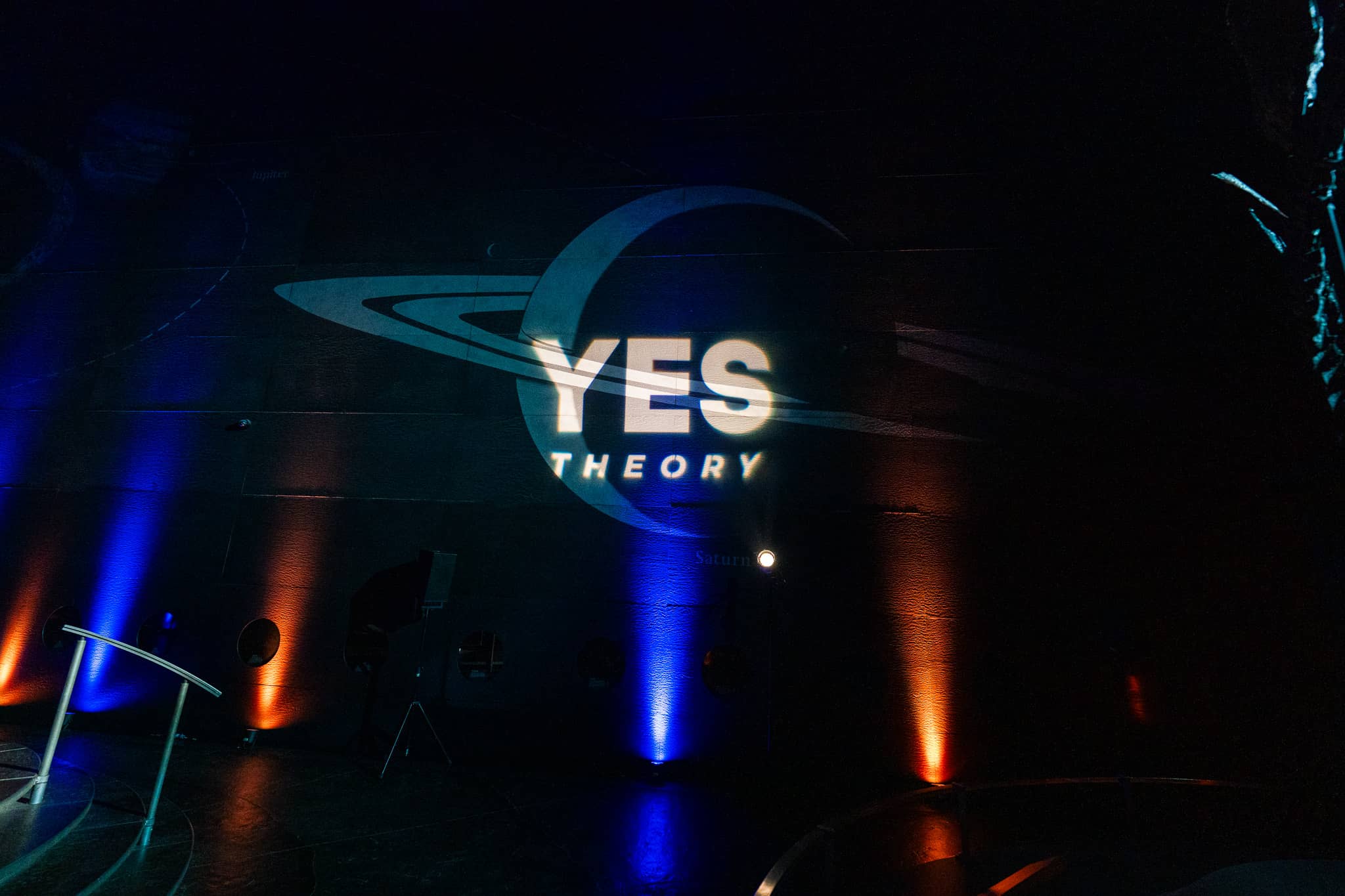 The Yes Theory logo projected by a custom gobo on the wall of Earth Hall, with blue and amber uplighting on the columns, by Kudos AV.