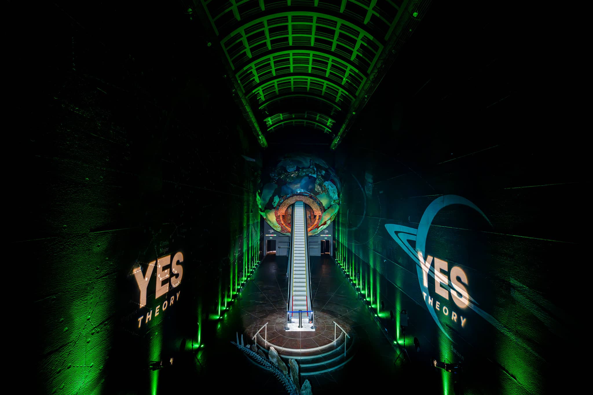 The escalator and the lit Earth sculpture in Earth Hall under green lighting at the Yes Theory 10 million subscriber celebration, by Kudos AV.