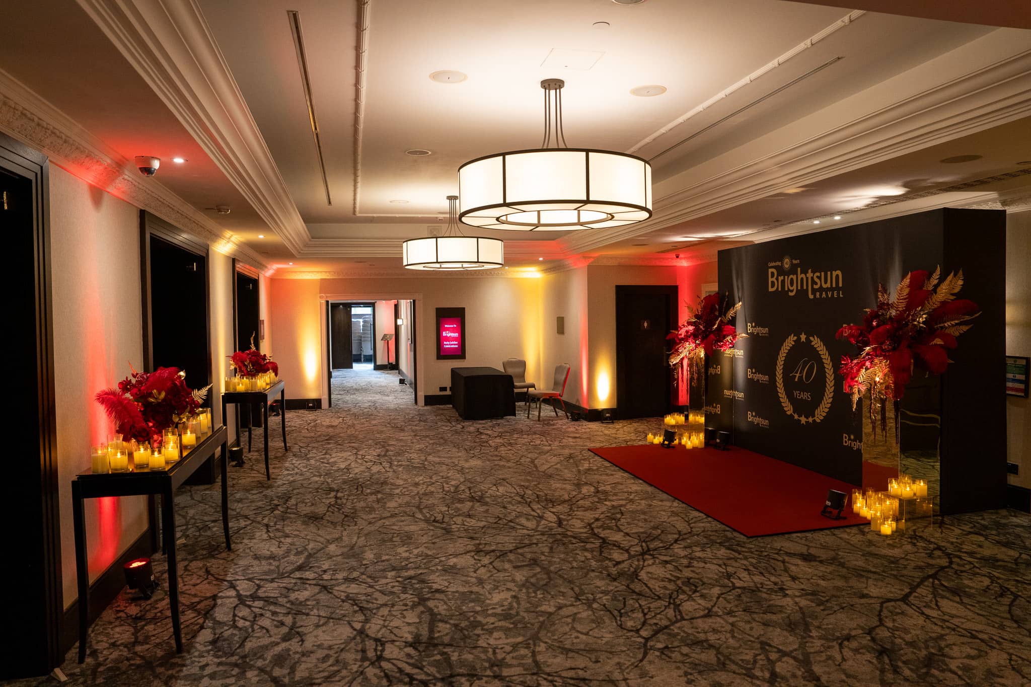 Foyer arrival route with the anniversary media wall and red and amber uplighting, at Brightsun Travel’s 40th anniversary at InterContinental London Park Lane.