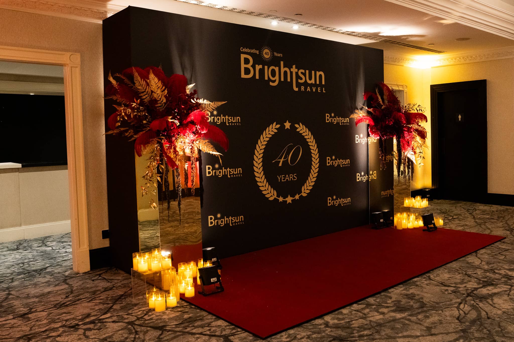 Angled view of Brightsun’s black and gold anniversary media wall with red carpet and warm uplighting, at Brightsun Travel’s 40th anniversary at InterContinental London Park Lane.