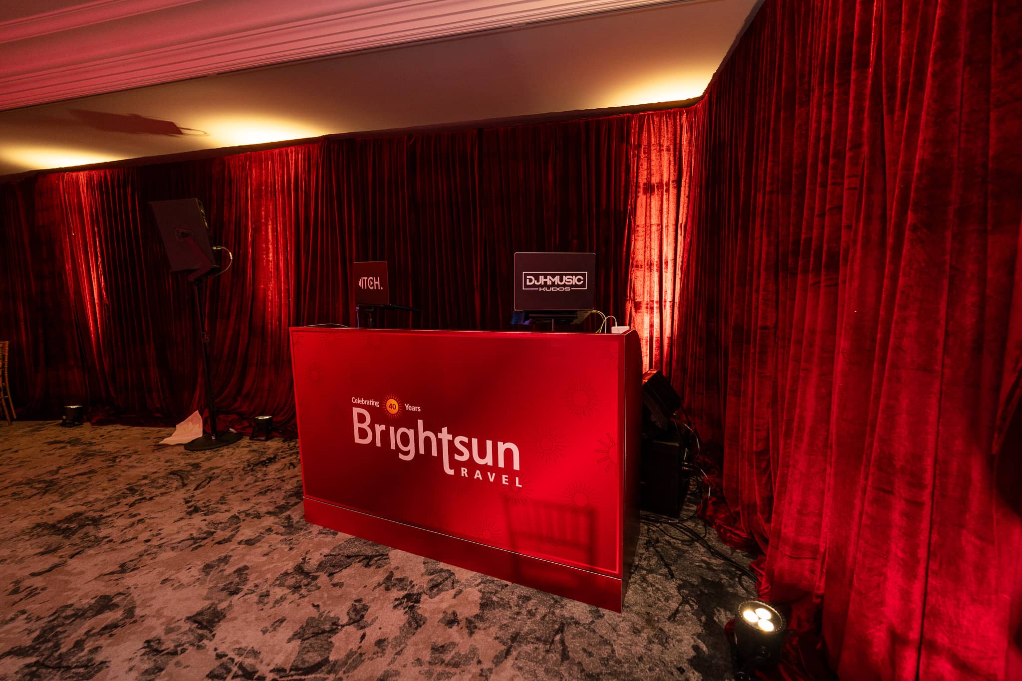 A red Brightsun-branded DJ booth set against red draping, at Brightsun Travel’s 40th anniversary at InterContinental London Park Lane.