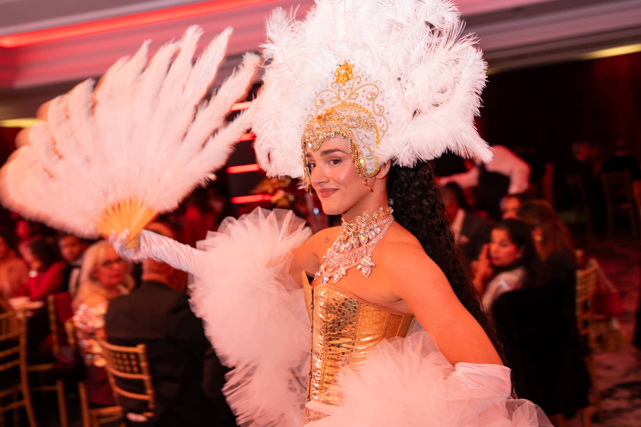 Showgirl in a white feathered headdress and gold costume under warm event lighting, at Brightsun Travel’s 40th anniversary at InterContinental London Park Lane.