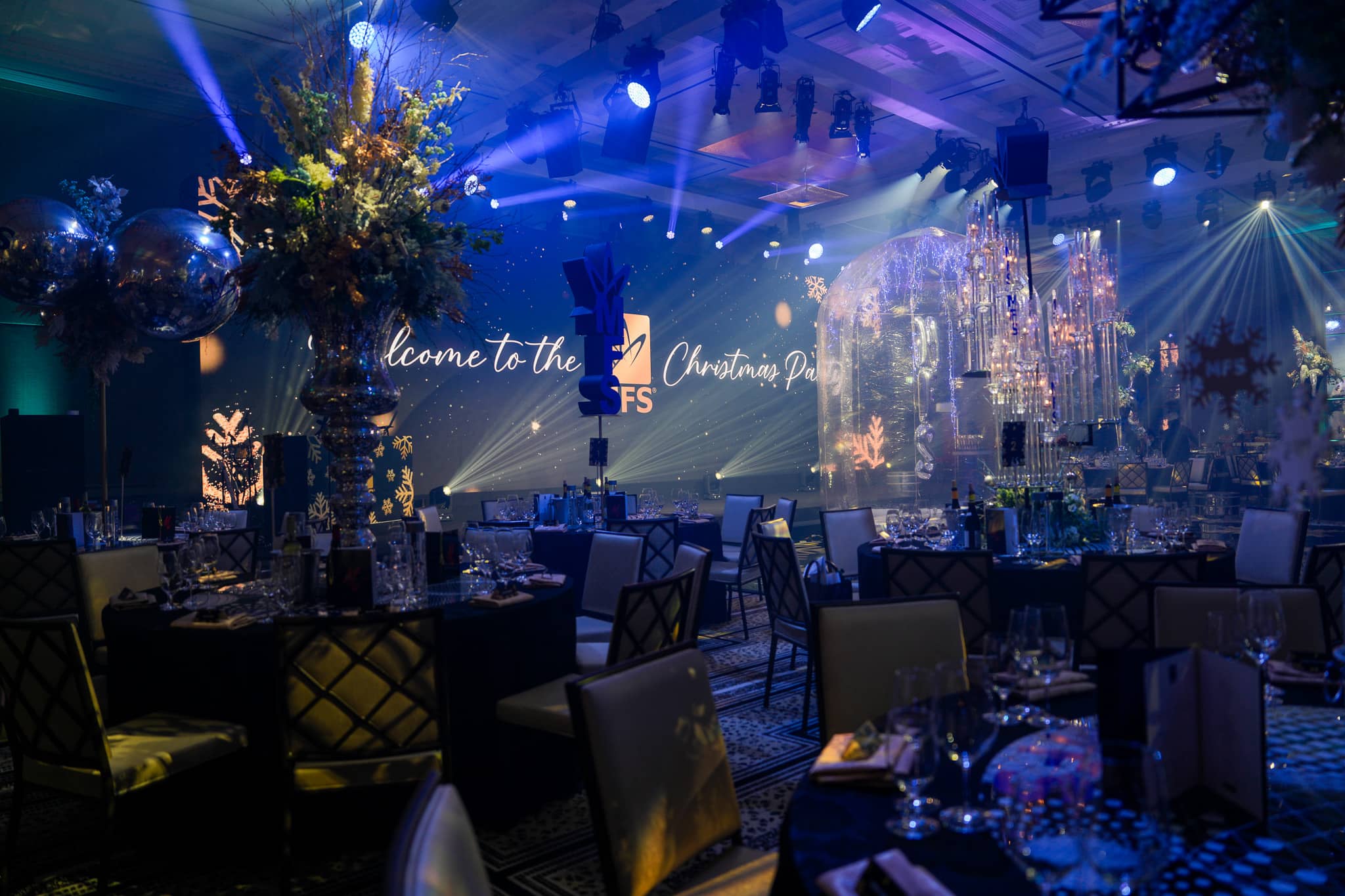Dinner tables facing the MFS Christmas party screen, with blue washes and white beams at The Peninsula London