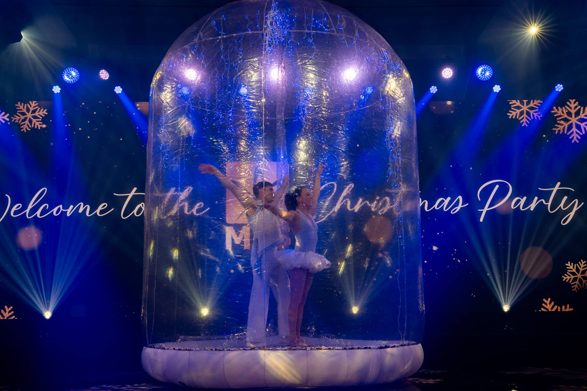 A performer inside a clear snow globe in front of the MFS Christmas party screen