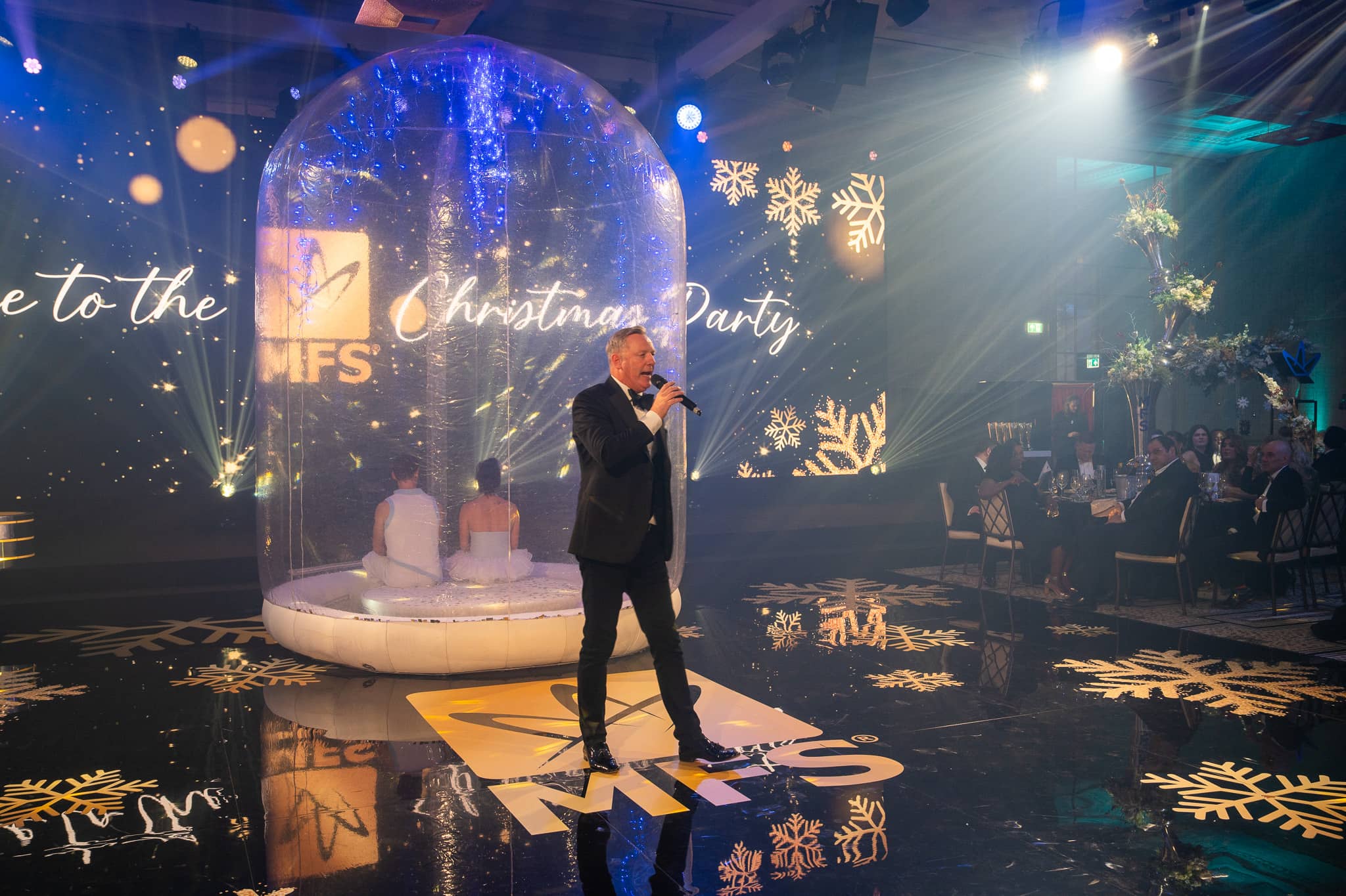 A singer stands above the gold MFS logo on the printed dancefloor with the snow globe behind