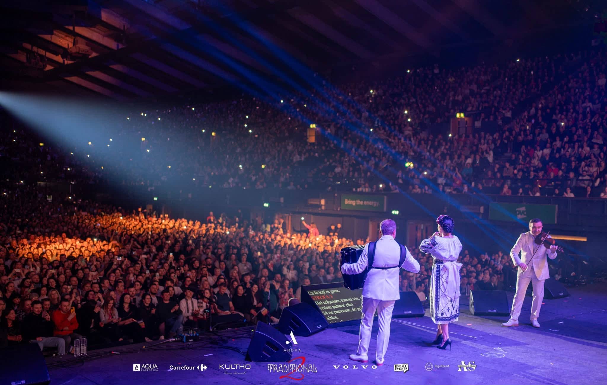 Andra with accordion and violin at the front of stage, blue beams fanning over a full arena, Andra Traditional 2 at OVO Arena Wembley, production by Kudos AV.