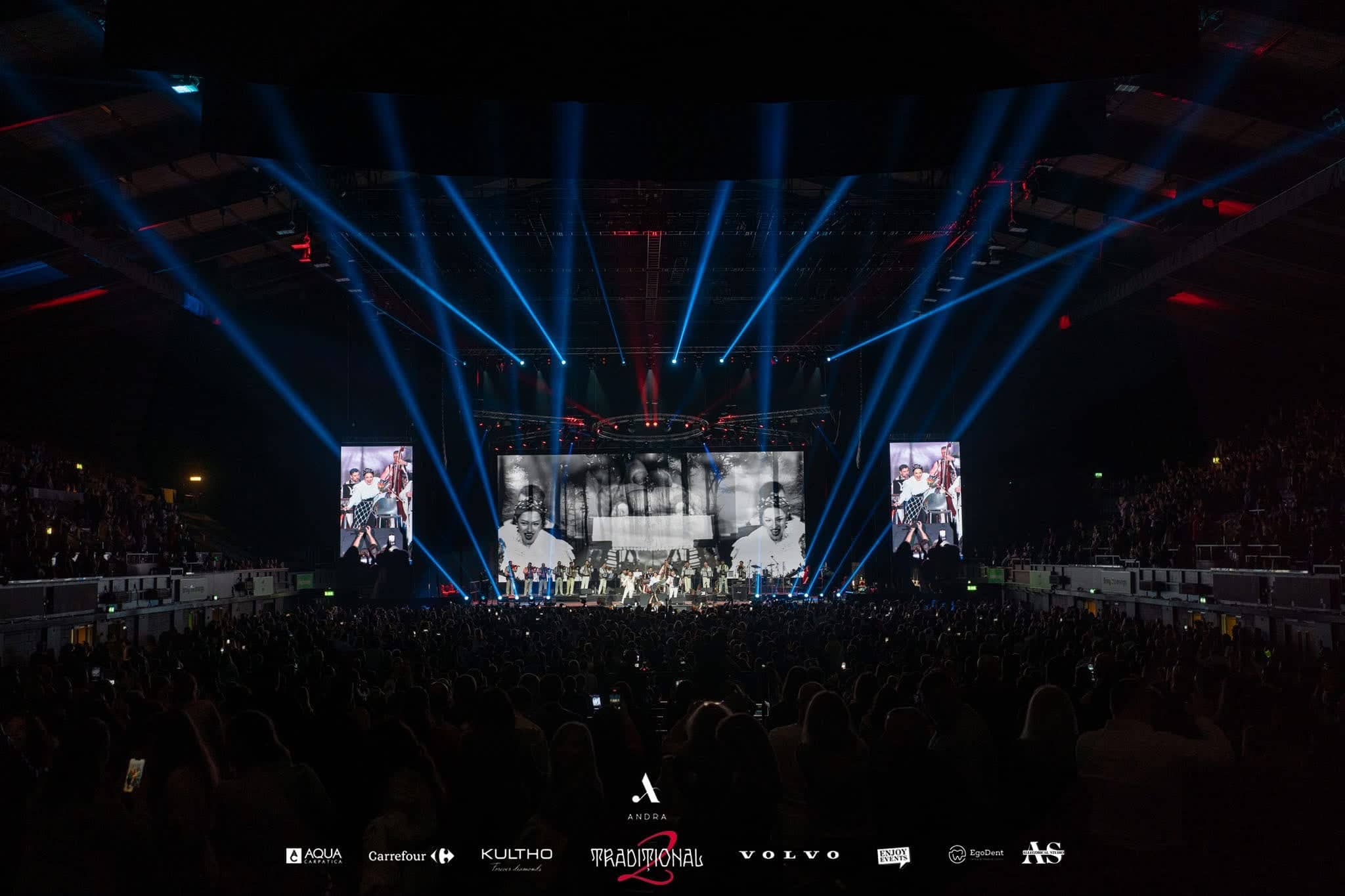 The full arena stage from the back of the room: a 17m LED main screen, two portrait IMAG screens and blue beams from the overhead rig, Andra Traditional 2 at OVO Arena Wembley, LED screens, lighting and sound by Kudos AV.