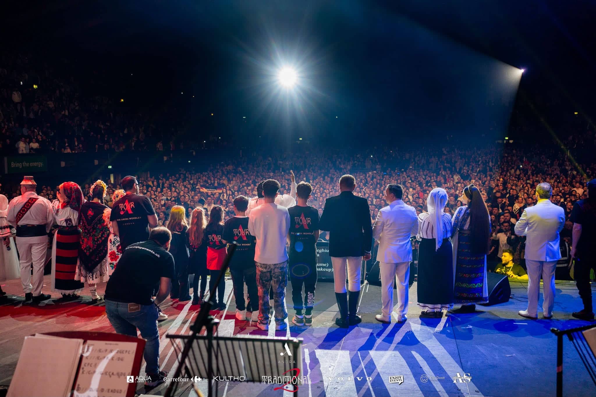 The cast and crew lined up across the stage facing the audience at the finale, a followspot from the back of the arena, Andra Traditional 2 at OVO Arena Wembley, production by Kudos AV.
