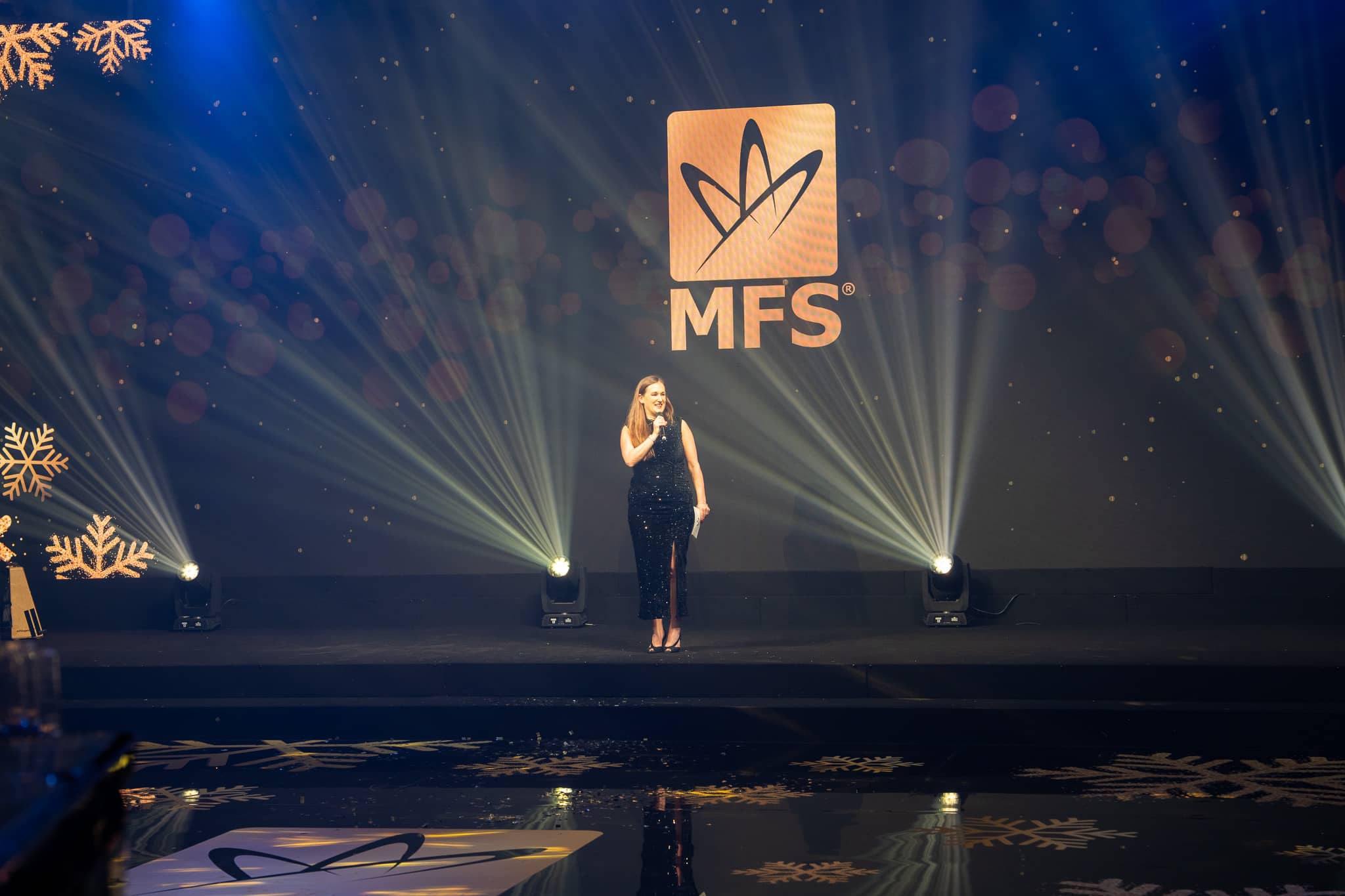 A presenter with a microphone on the lit MFS awards stage at The Peninsula London