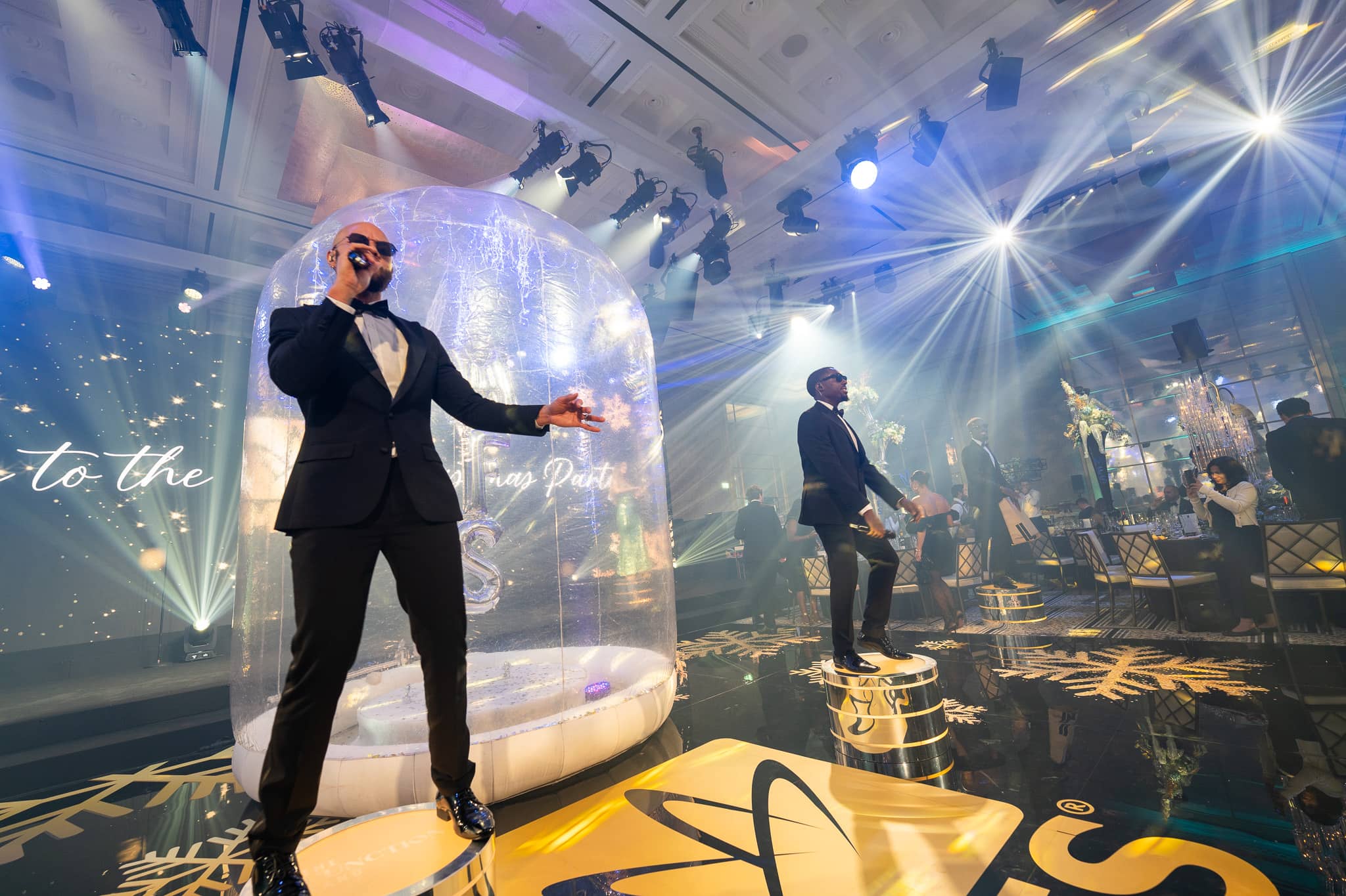 A vocalist performs in front of the snow globe as white beams cross the MFS ballroom