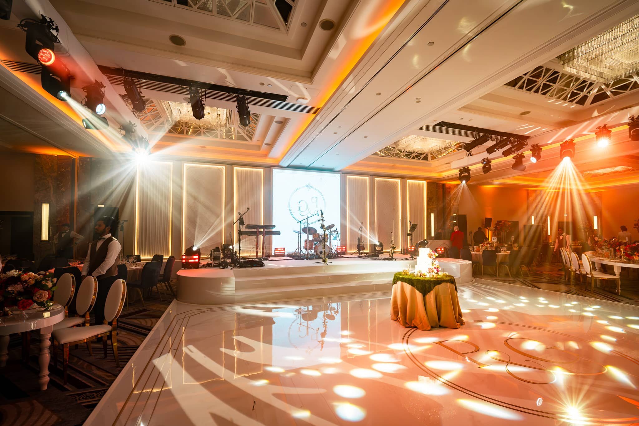 Wide view of overhead beams, white dancefloor and the illuminated stage set at Royal Lancaster London.
