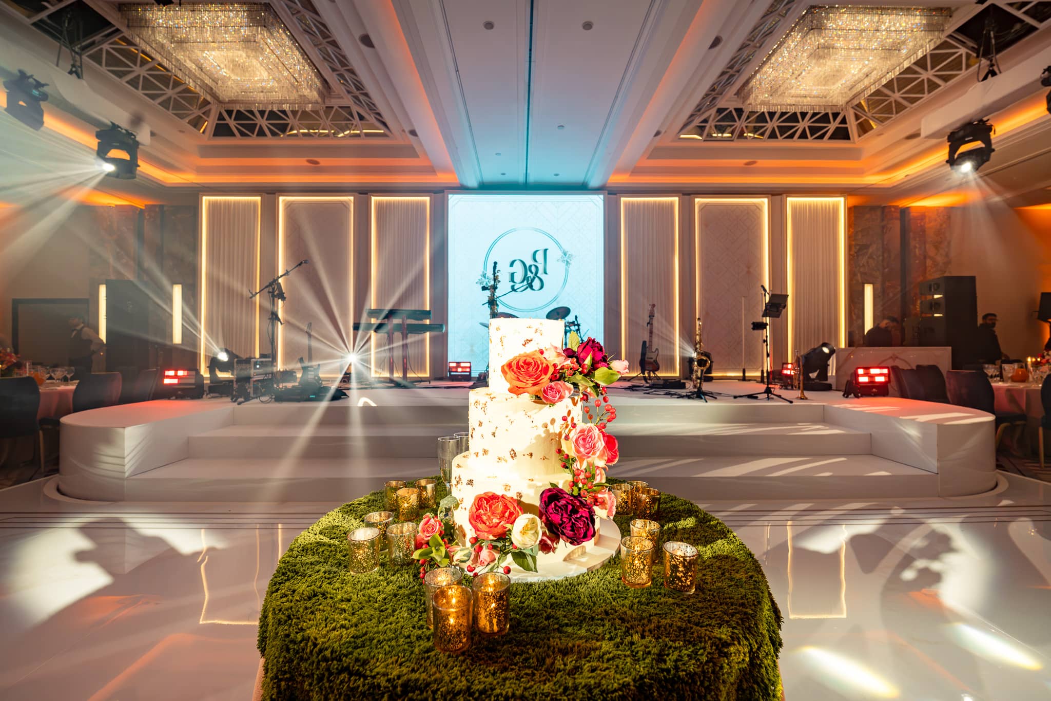 Wedding cake on a green-covered table in front of the bespoke dancefloor and LED-backed stage.
