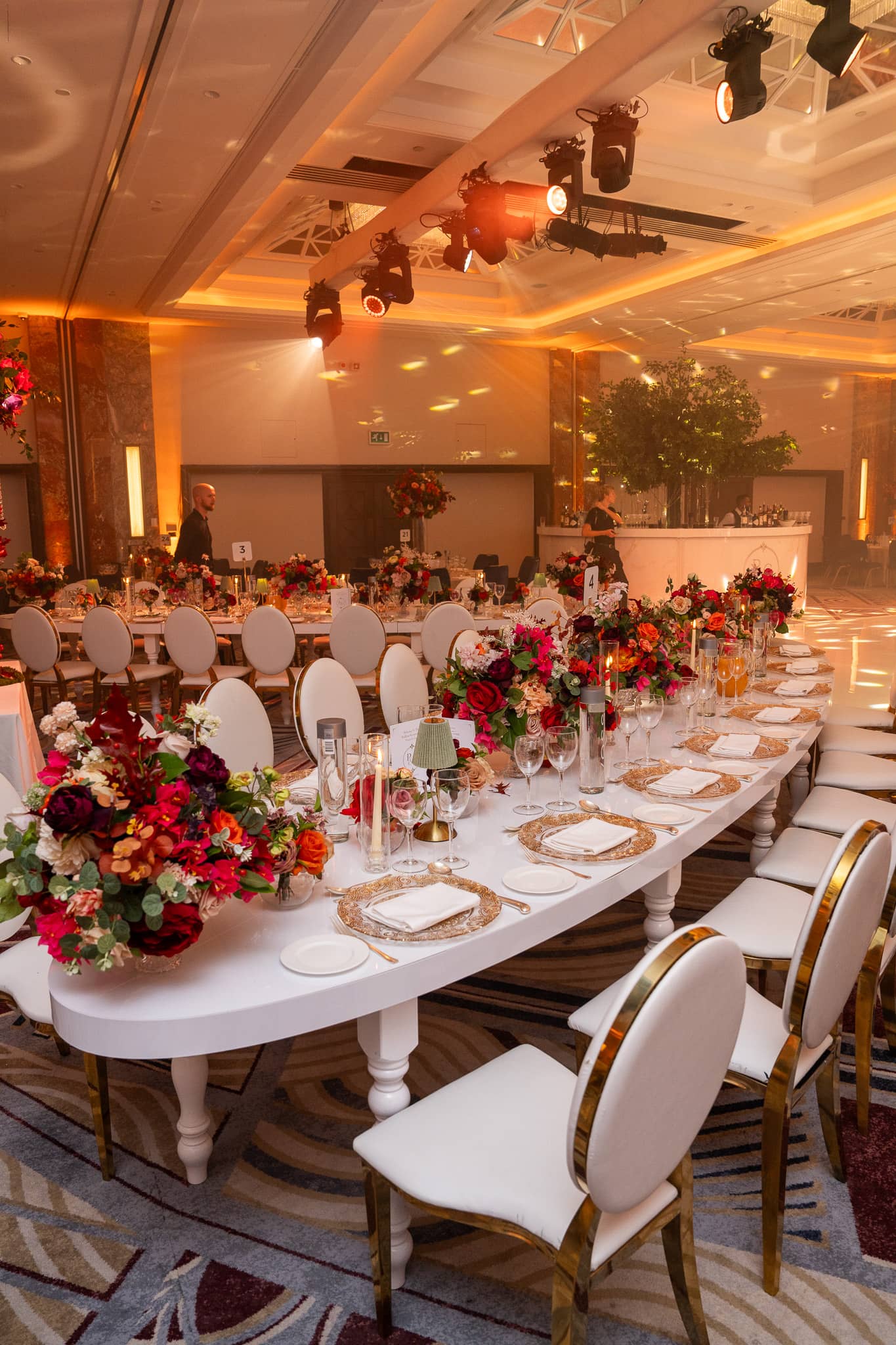 Portrait view of a white curved dining table and overhead lighting beside the wedding dancefloor.