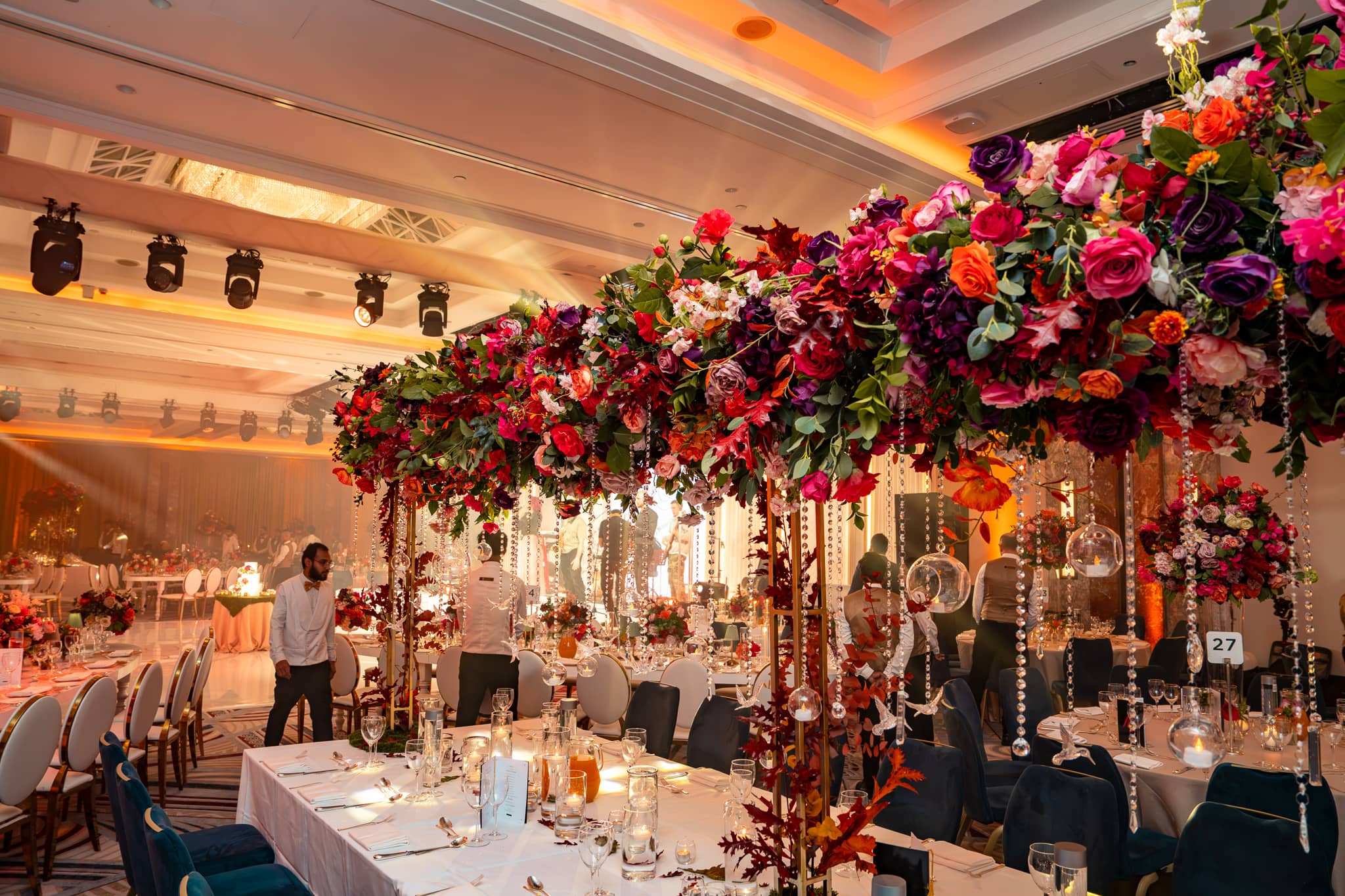 Floral canopy over a banquet table with overhead production lights visible across the ballroom ceiling.