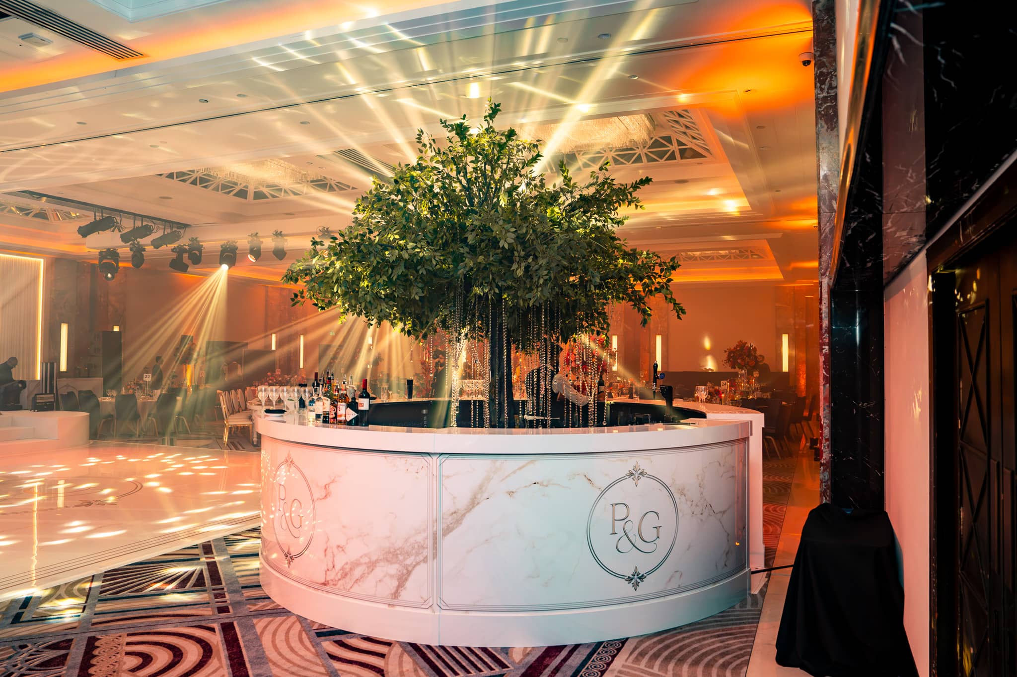Round printed bar with Pooja and Gary’s monogram and pale marble-effect artwork beneath a tree centrepiece.