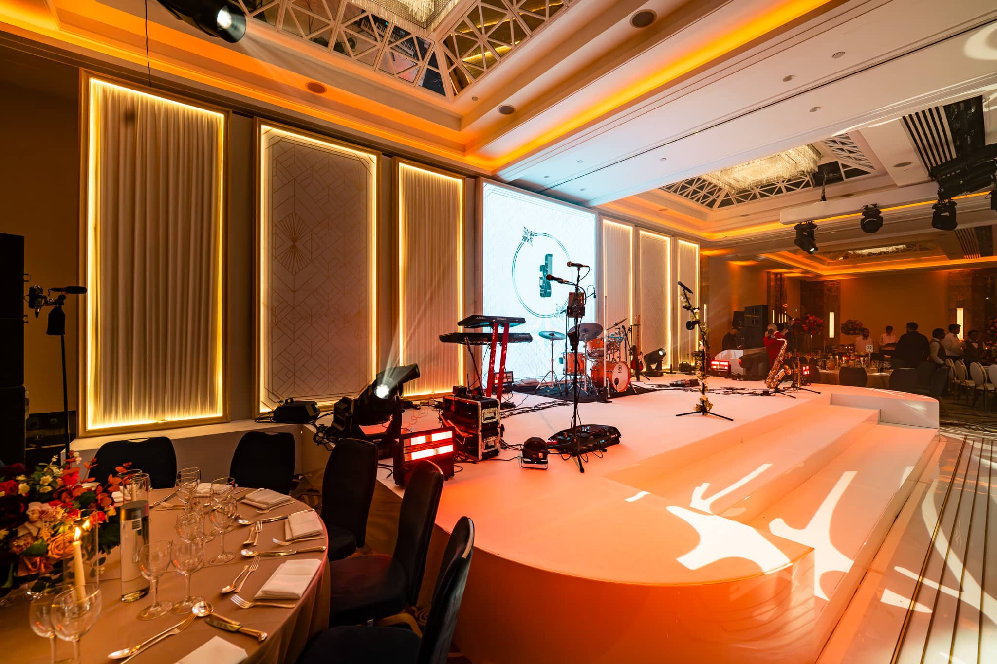 Side view of the white stage, central monogram LED screen and tall set panels edged with warm light.