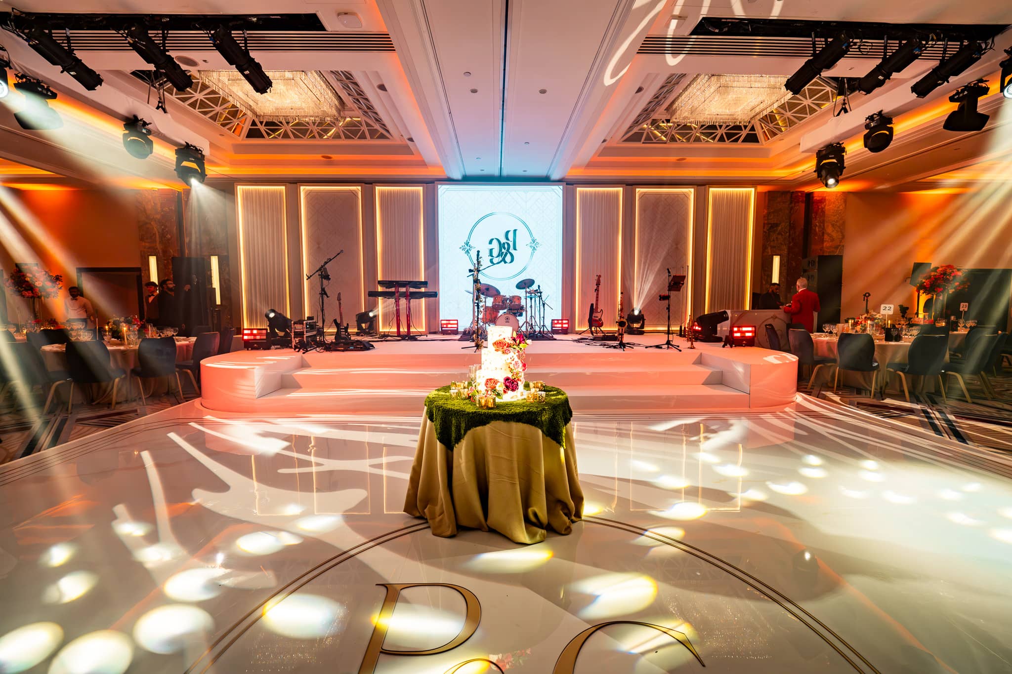 Front view across the monogrammed dancefloor towards the white stepped stage, central LED screen and lit set panels.