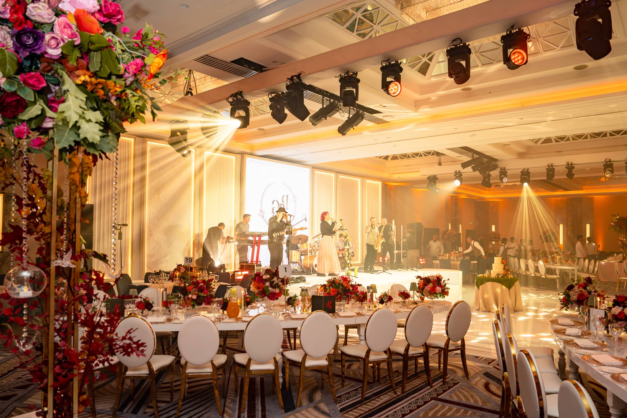 Golden overhead beams above the stage and dining tables during Pooja and Gary’s reception.