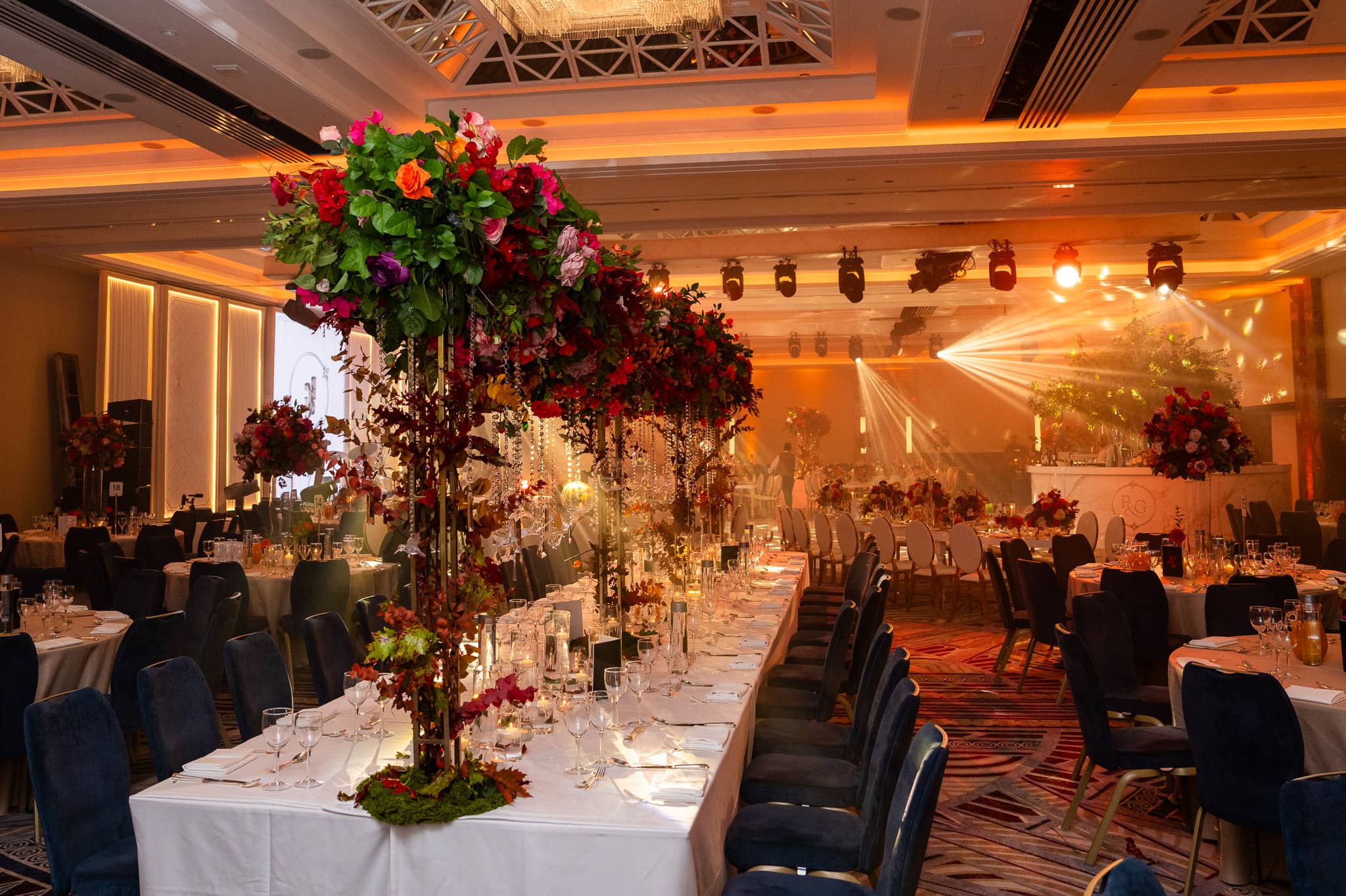 Overhead lighting beams above long dining tables and floral displays at Royal Lancaster London.