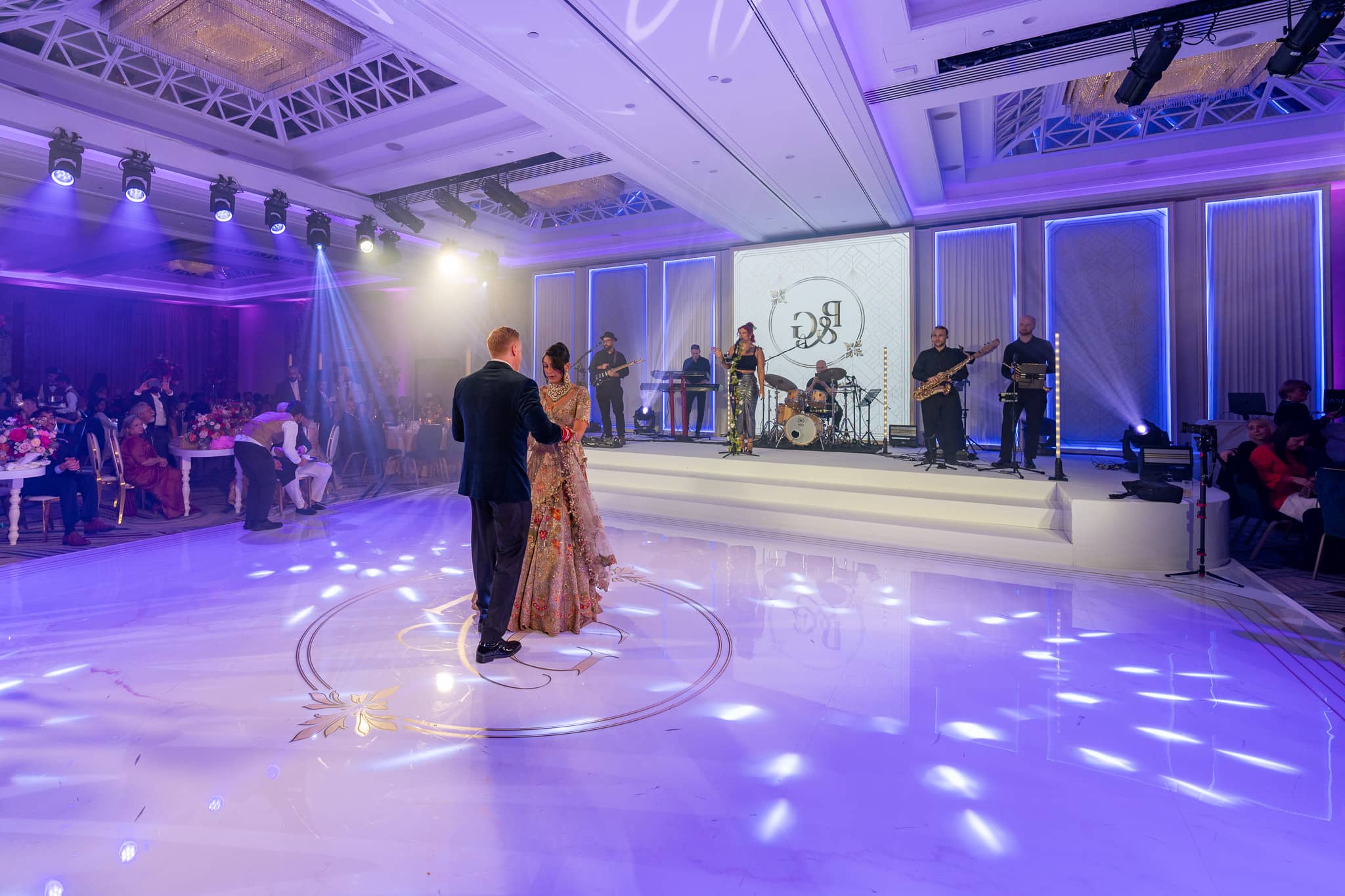 Pooja and Gary on their monogrammed dancefloor under purple light, with the stage and LED screen behind.