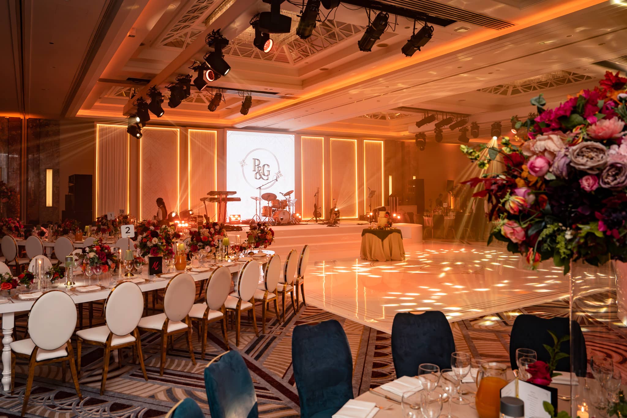Bespoke white dancefloor, central LED screen and illuminated set panels viewed past the dining tables.