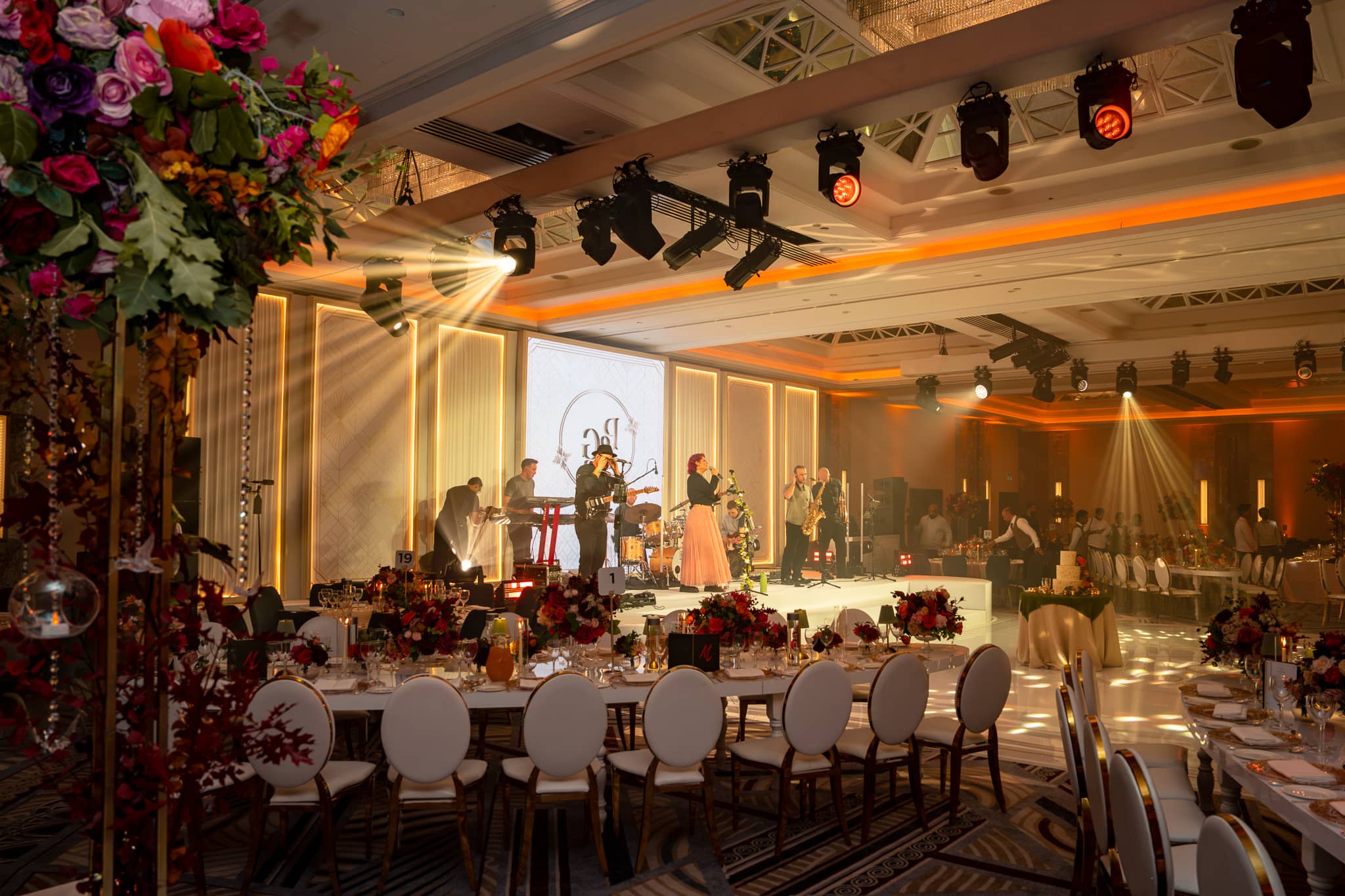 View past a floral canopy towards performers on the LED-backed stage under warm beams.