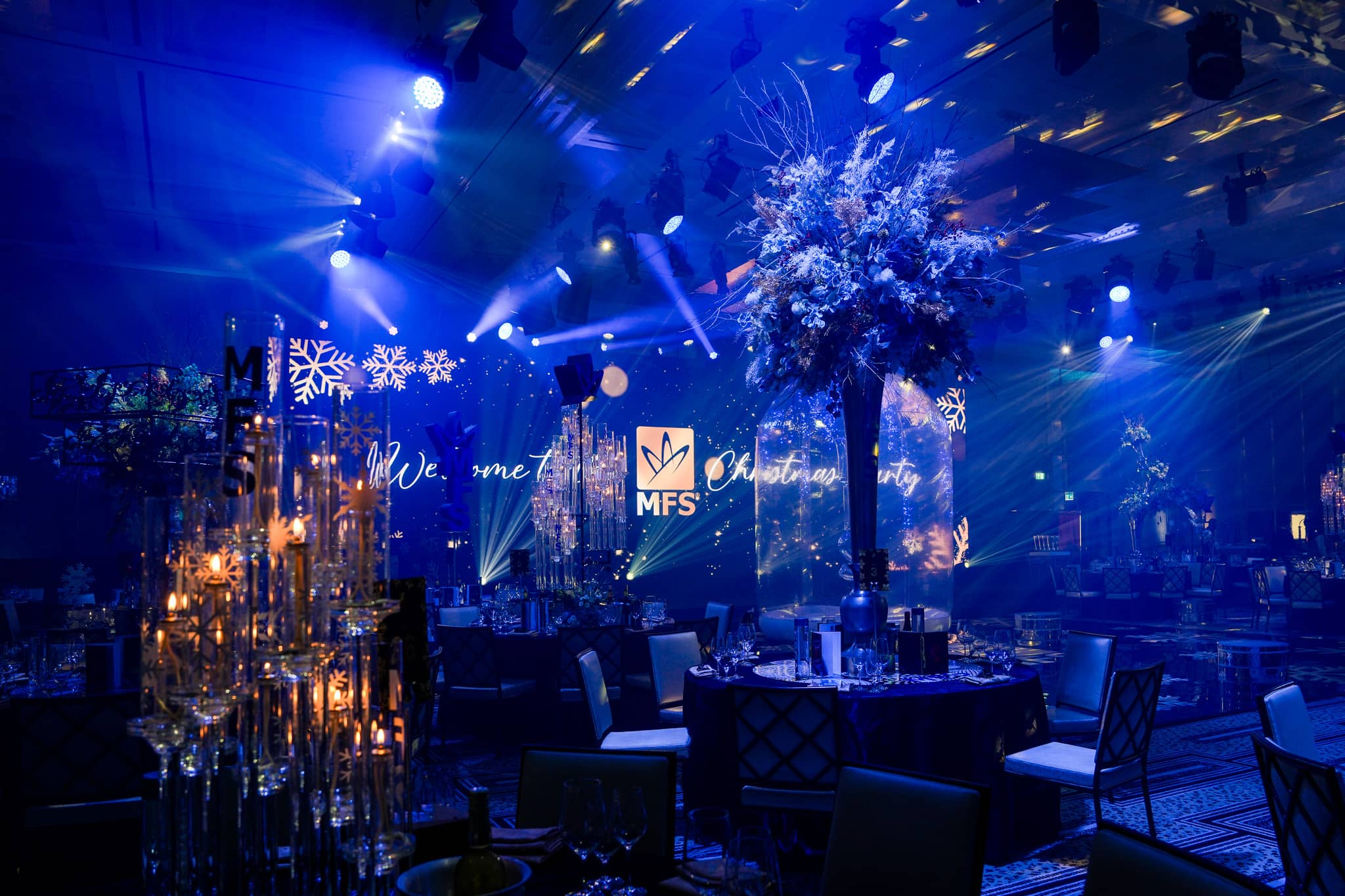 Candlelit table details and tall floral centrepieces beneath blue light at the MFS Christmas party