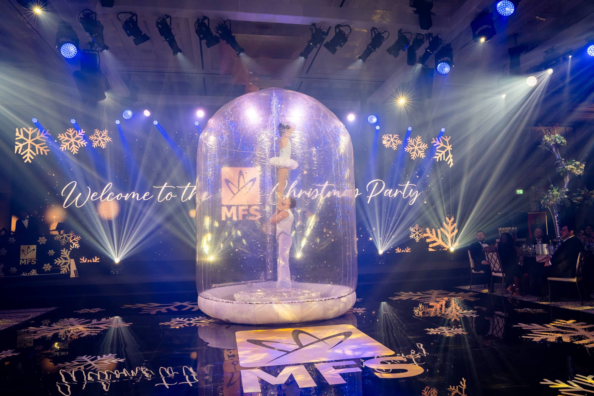 A performer inside the illuminated snow globe, with gold snowflakes on the MFS screen and floor