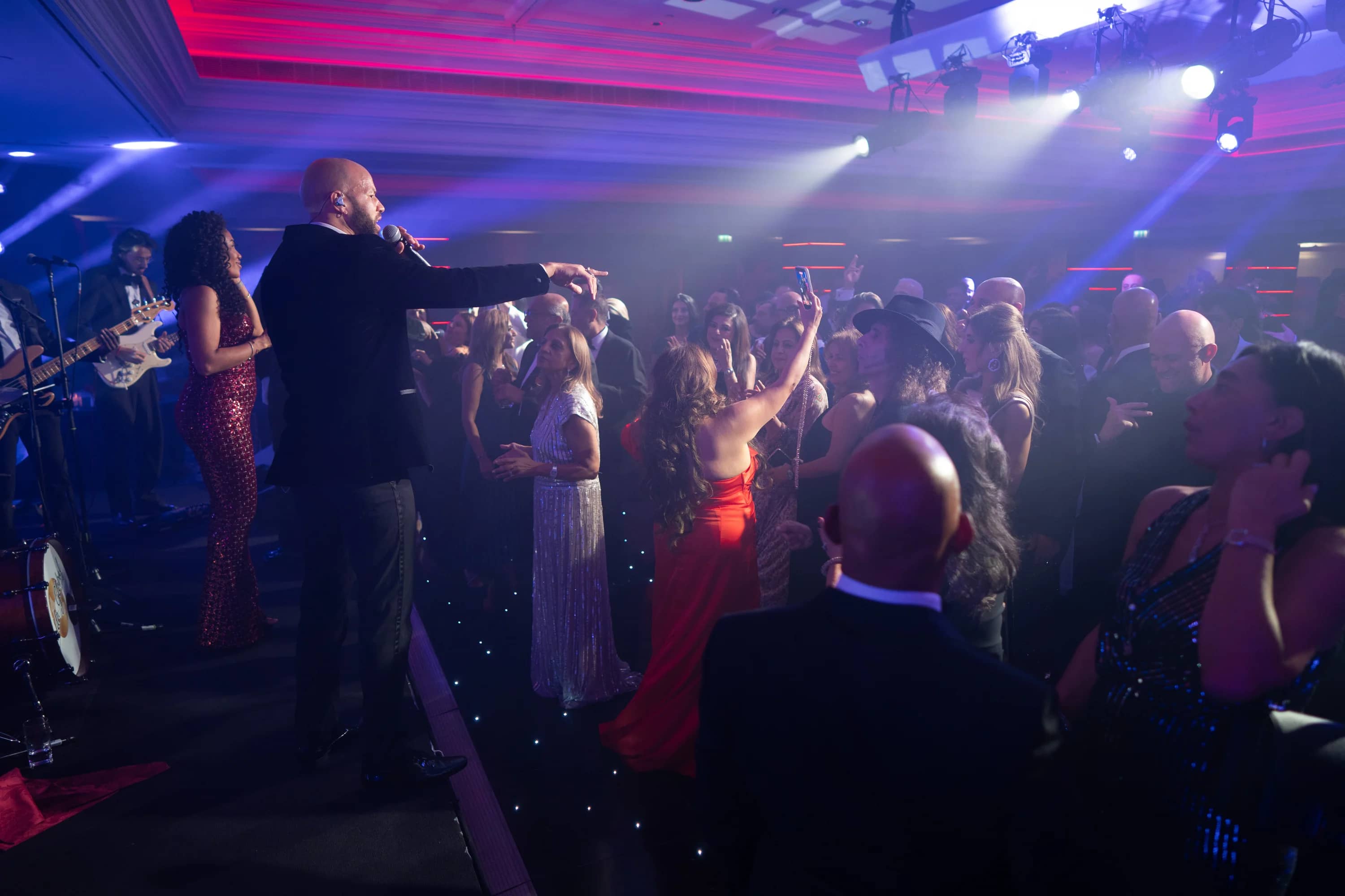 A performer with a microphone leading the crowd under blue and white stage beams, at Brightsun Travel’s 40th anniversary at InterContinental London Park Lane.