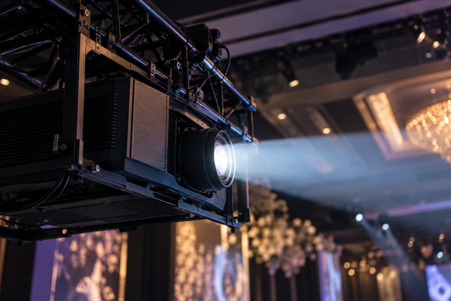 Laser projector rigged on truss, its beam crossing a chandelier ballroom at a corporate event produced by Kudos AV